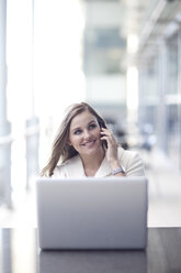 Young businesswoman using laptop and chatting on smartphone in conference centre - CUF32813