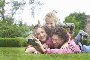 Father photographing family lying on lawn - CUF32899