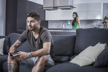 Young man on sofa using gaming control watched by angry girlfriend - CUF32960