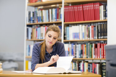 Junge Studentin beim Lesen eines Lehrbuchs am Bibliotheksschalter - CUF32990