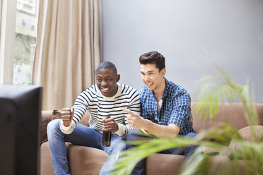 Zwei junge Männer trinken Bier und sehen im Wohnzimmer fern - CUF33056