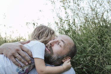 Father and little daughter lying together on a meadow hugging each other - KMKF00359