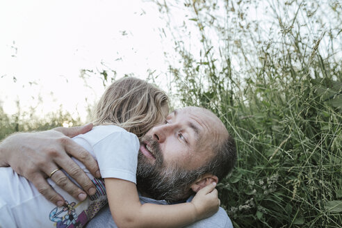 Vater und kleine Tochter liegen zusammen auf einer Wiese und umarmen sich - KMKF00359