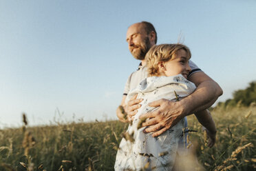 Father and son standing on a meadow hugging each other - KMKF00363