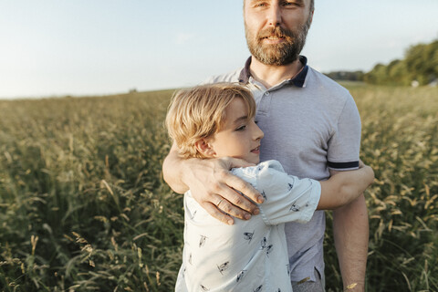 Father and son standing on a meadow hugging each other stock photo