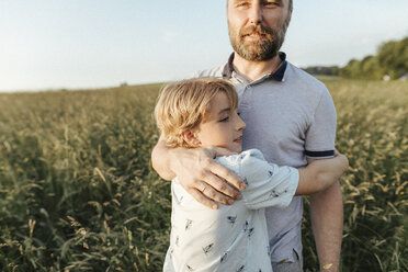 Father and son standing on a meadow hugging each other - KMKF00364