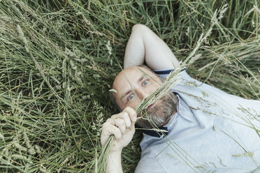 Porträt eines reifen Mannes, der im Gras liegt und komische Gesichter zieht - KMKF00371