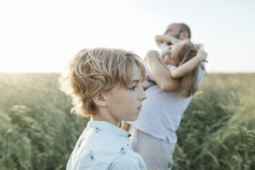 Trauriger Junge mit Vater und Schwester, die im Hintergrund zusammen spielen - KMKF00373