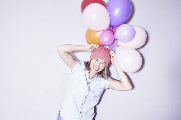 Studio shot of young woman holding bunch of balloons on head - CUF33145