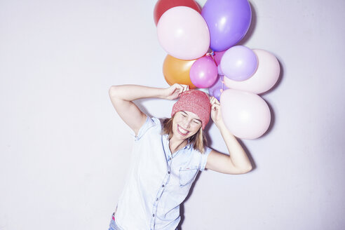 Studioaufnahme einer jungen Frau, die ein Bündel Luftballons auf dem Kopf hält - CUF33145