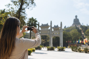 Junge Touristin fotografiert mit ihrem Smartphone den Tian-Tan-Buddha, Po-Lin-Kloster, Lantau Island, Hongkong, China - CUF33160