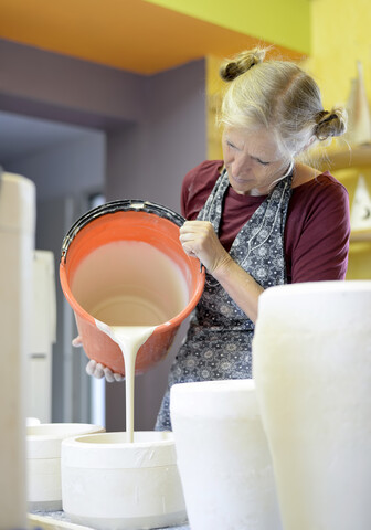 Frau gießt Flüssigkeit in eine Form in einer Porzellanwerkstatt, lizenzfreies Stockfoto
