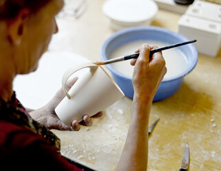 Frau mit Pinsel auf Tasse in Porzellanwerkstatt - BFRF01860