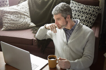 Young man drinking coffee and browsing laptop - ISF10664