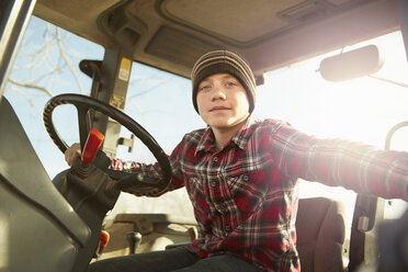 Portrait of boy farmer driving tractor on dairy farm - ISF10673