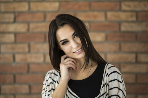 Porträt einer lächelnden jungen Frau mit langen braunen Haaren vor einer Backsteinmauer, lizenzfreies Stockfoto