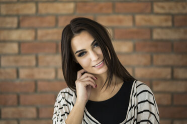 Porträt einer lächelnden jungen Frau mit langen braunen Haaren vor einer Backsteinmauer - AWF00055