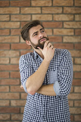 Portrait of bearded young man in front of brick wall thinking - AWF00058