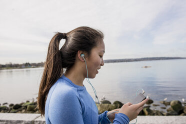 Junge Frau mit Kopfhörern und mp3-Player in der Hand, English Bay, Vancouver, Kanada - ISF10699