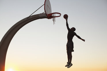 Young man with basketball, jumping towards net, outdoors - ISF10725