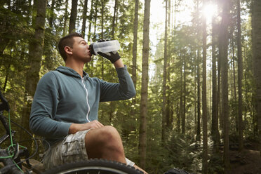 Young man with mountain bike in forest, taking drink from water bottle - ISF10729