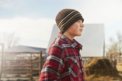 Porträt eines Jungen mit Strickmütze auf dem Hof eines Milchviehbetriebs, lizenzfreies Stockfoto