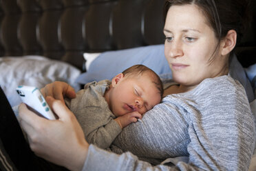 Junge Frau mit Smartphone, Baby schläft auf ihrer Brust - ISF10755