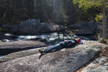Male hiker lying on riverside rock, Rangeley, Maine, USA - ISF10758