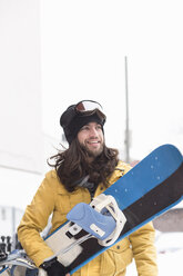 Lächelnder männlicher Snowboarder mit Snowboard auf der Straße - ISF10789
