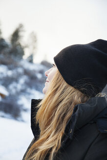Mittlere erwachsene Frau mit Strickmütze blickt auf eine verschneite Landschaft - ISF10817