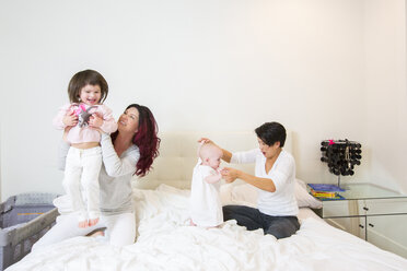 Female couple on bed having fun with baby and toddler daughters - ISF10855