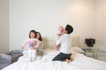 Female couple on bed playing with baby and toddler daughters - ISF10856