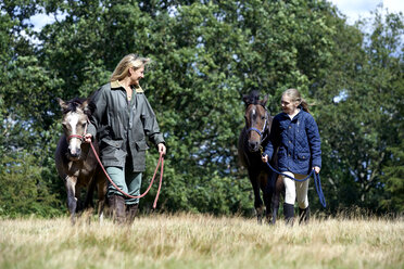 Mutter und Tochter gehen mit Pferden im Feld spazieren - ISF10872