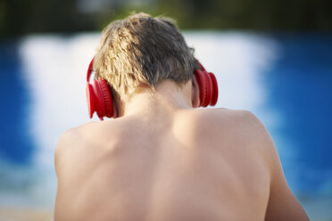 Rear head and shoulder view of teenage boy wearing headphones at poolside - ISF10948