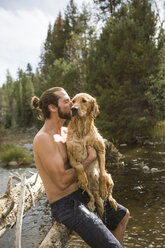 Young man kissing his wet dog at river, Lake Tahoe, Nevada, USA - ISF10958