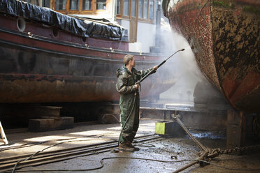 Worker cleaning boat with high pressure hose in shipyard - ISF10989