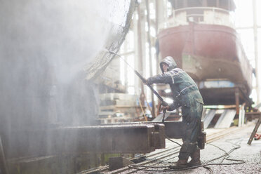 Arbeiter mit Hochdruckschlauch an einem Boot in einer Werftwerkstatt - ISF11006