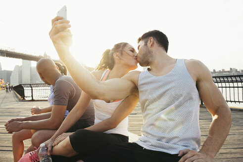 Junges erwachsenes laufendes Paar, das sich für ein Smartphone-Selfie am Flussufer küsst, New York, USA - ISF11088