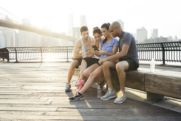 Vier erwachsene Lauffreunde lesen Smartphone-Text vor der Brooklyn-Brücke, New York, USA - ISF11091