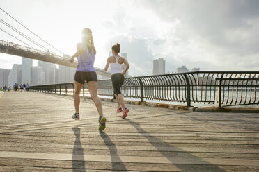 Two female running friends running in front of Brooklyn bridge, New York, USA - ISF11094