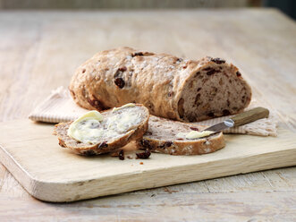 Aufgeschnittenes Sauerteigbrot mit Früchten und Nüssen, bestrichen mit Butter und Buttermesser - ISF11120