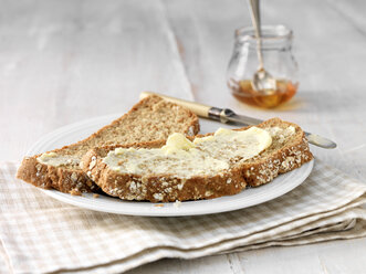 Butter smeared on wholemeal bread with butter knife and honey jar - ISF11122