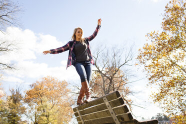 Young woman balancing on top of park bench in autumn forest - ISF11178