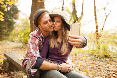 Junges Paar auf einer Bank nimmt Smartphone-Selfie im Herbst Wald - ISF11211