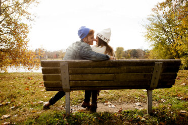 Rückansicht eines romantischen jungen Paares auf einer Parkbank am Seeufer - ISF11220