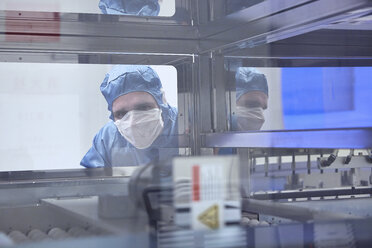 Männlicher Arbeiter schaut durch ein Maschinenfenster im Reinraum einer flexiblen Elektronikfabrik - ISF11245