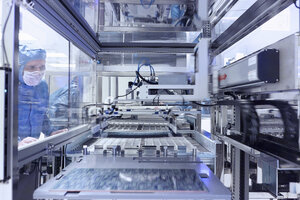 Male worker looking through window of manufacturing machinery in flexible electronics factory clean room - ISF11250