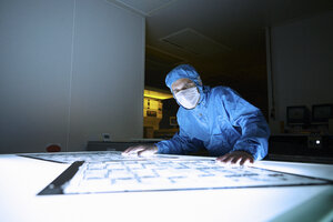 Male worker inspecting flex circuit on lightbox in flexible electronics factory clean room - ISF11269