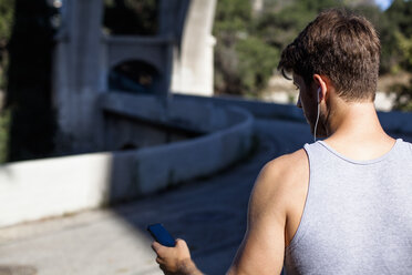 Jogger wählt Musik auf dem Smartphone aus, Arroyo Seco Park, Pasadena, Kalifornien, USA - ISF11335