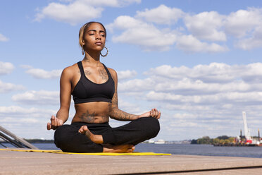 Junge Frau sitzt im Schneidersitz am Wasser in Yogastellung, Augen geschlossen, Philadelphia, Pennsylvania, USA - ISF11354